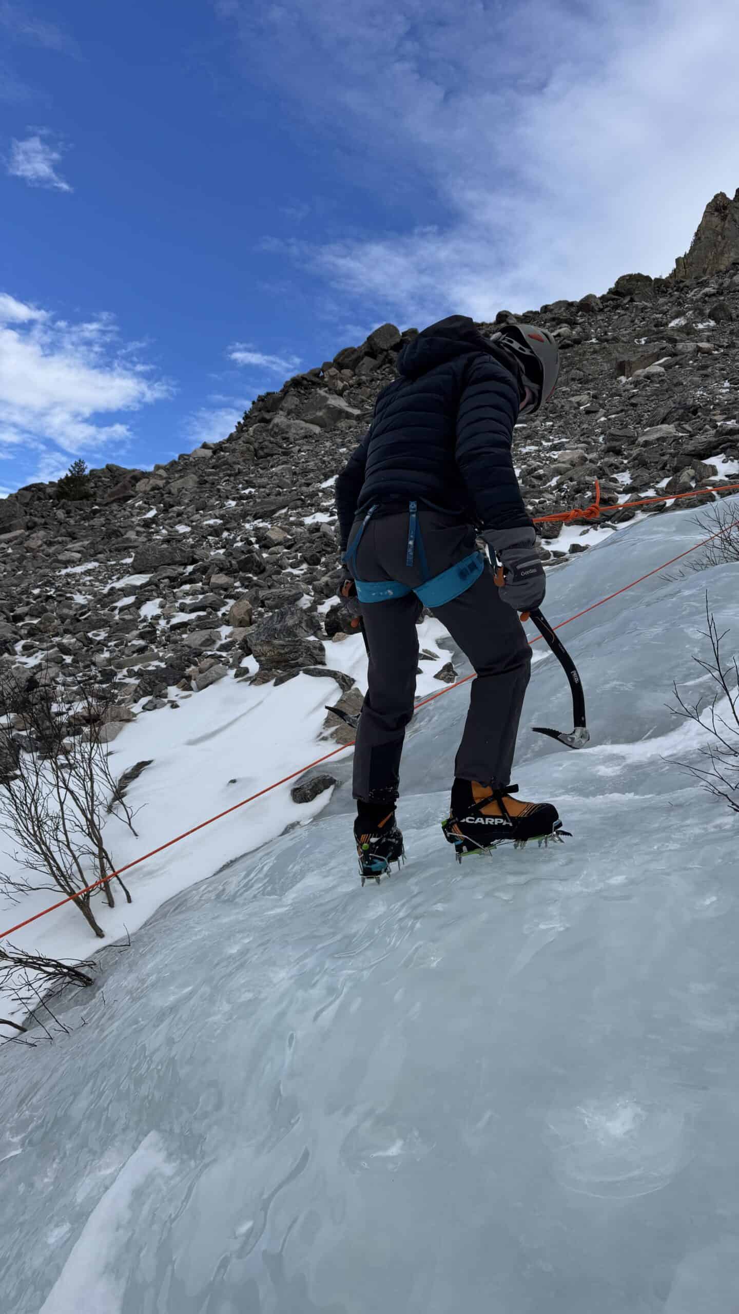 Climber front-pointing up a frozen ice slope with an ice axe during a Basic Mountaineering Course
