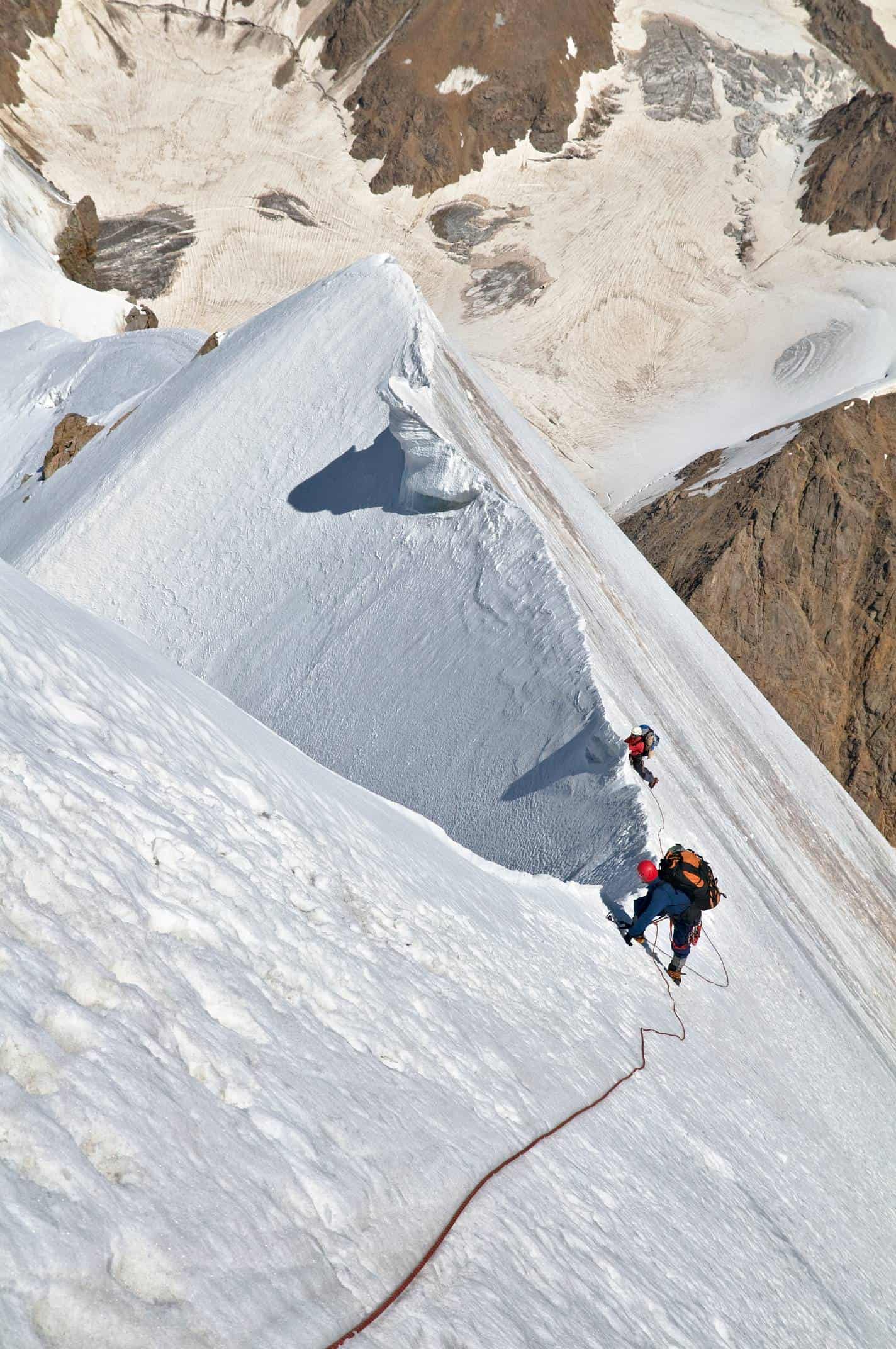 Two roped climbers moving along an exposed snow ridge during Alpine Pro-1 in Kyrgyzstan