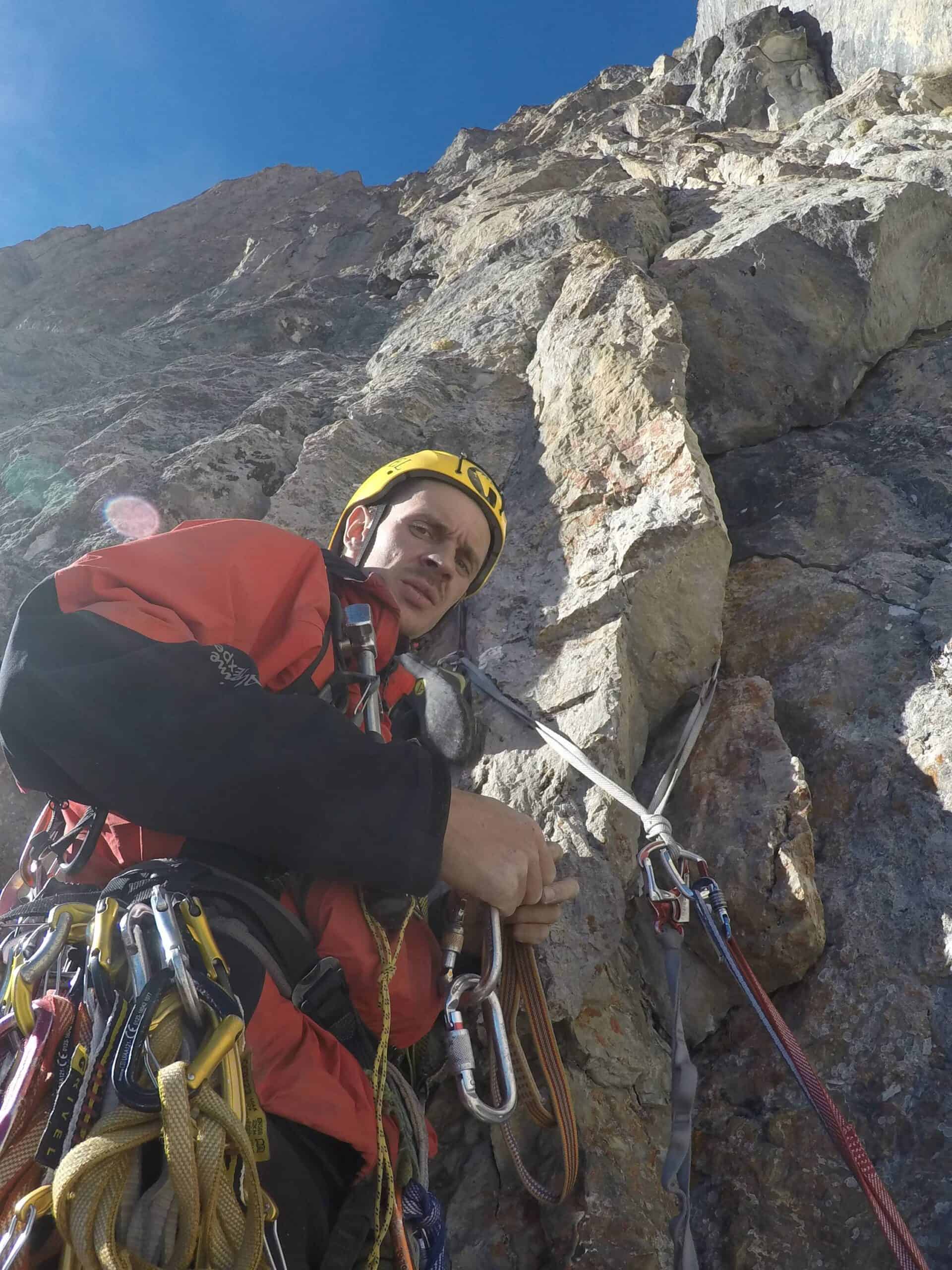Climber building a multi-point rock anchor on a sunny alpine wall during Alpine Pro-1