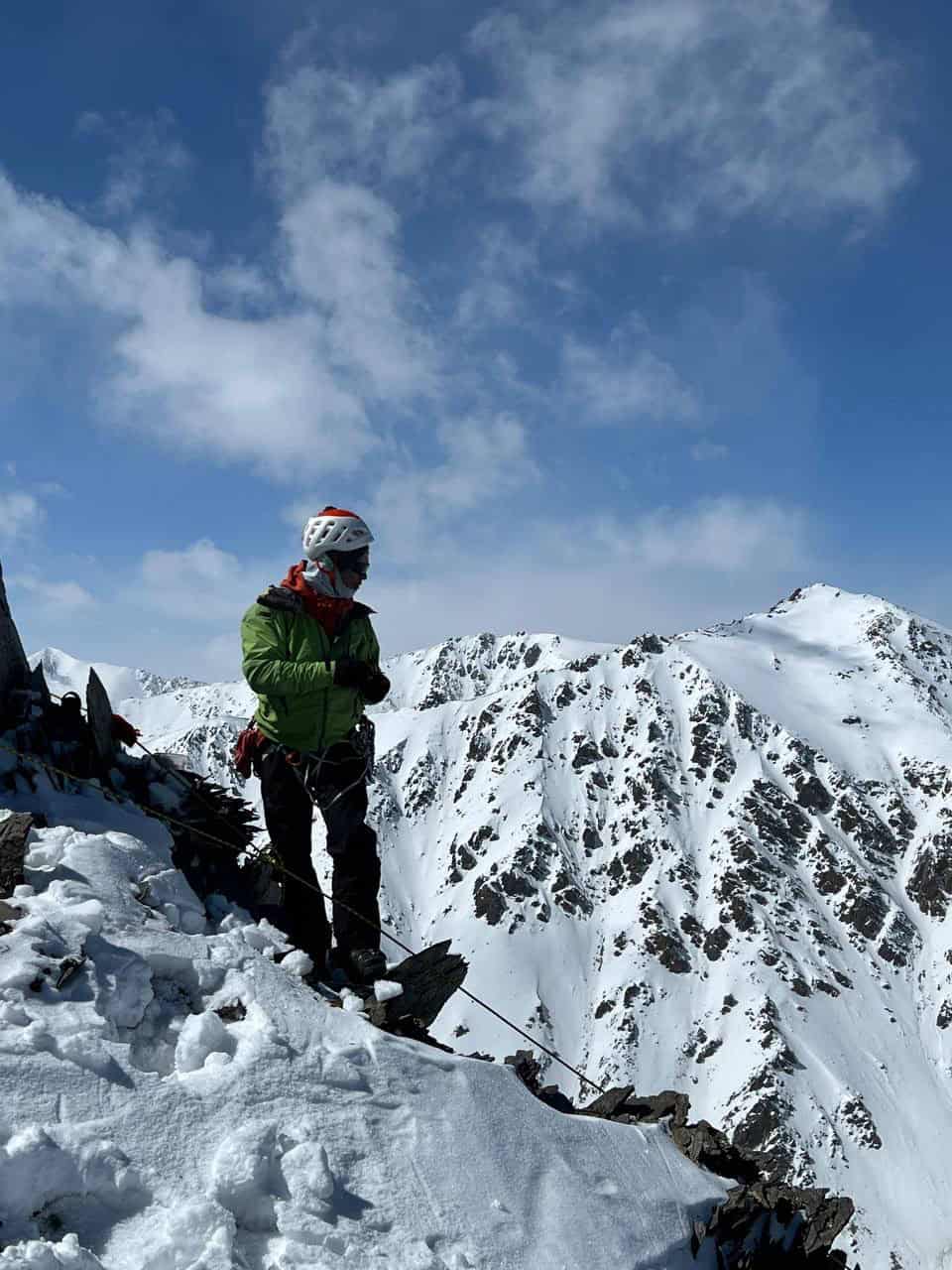 Climber pausing on a snowy summit ridge overlooking the Ala-Archa range during Alpine Pro-1
